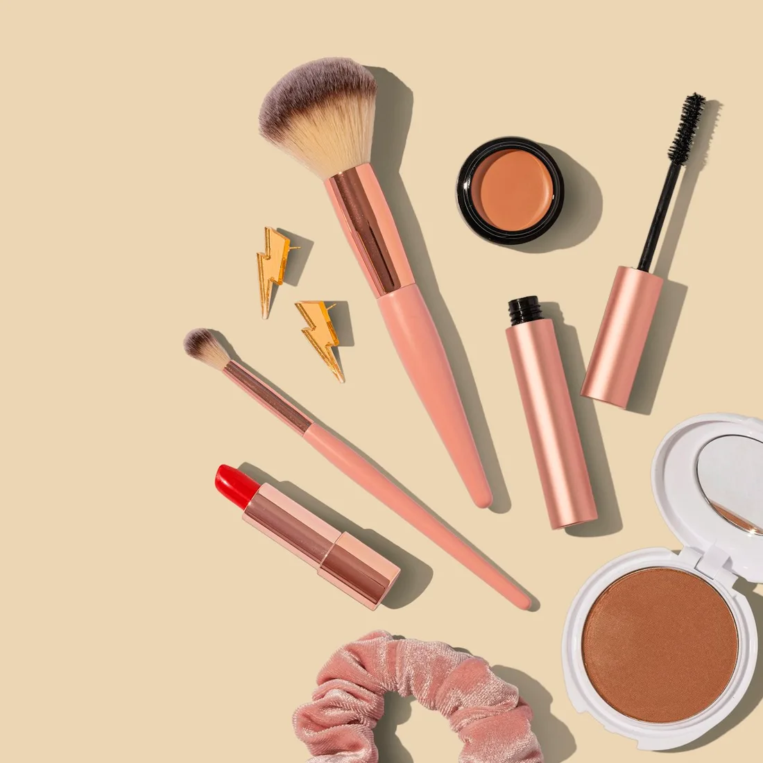 Small makeup containers and tools laid out against a peach backdrop